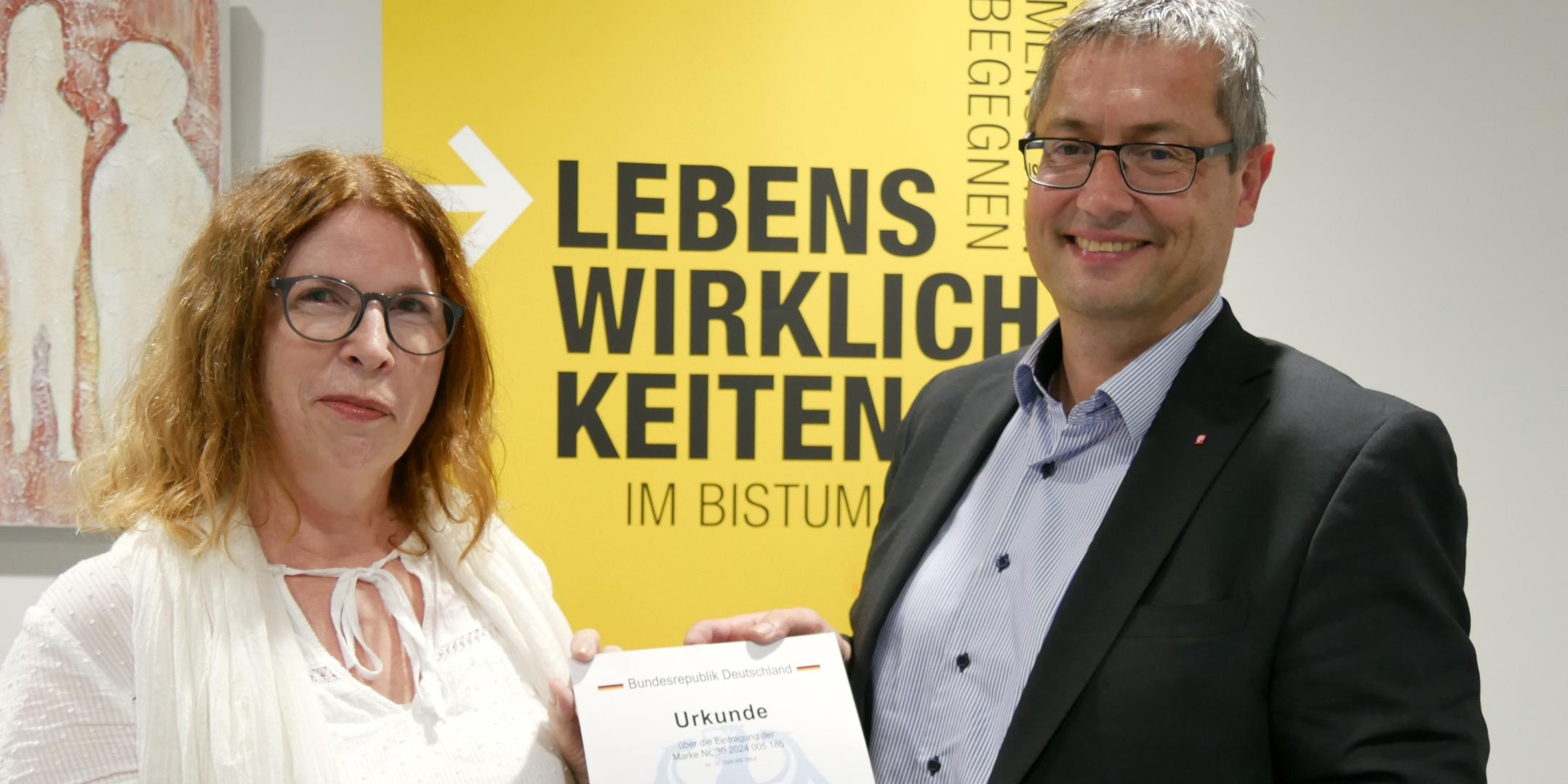 Dr. Martina Messan (Programmleiterin) und Diözesan-Caritasdirektor Christoph Wutz präsentieren stolz die Urkunde zur Markeneintragung.