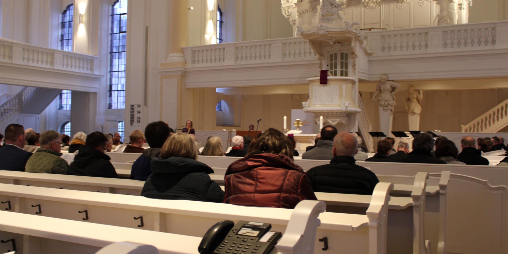 Menschen sitzen in den Kirchenbänken, auf den Bänken stehen Telefone