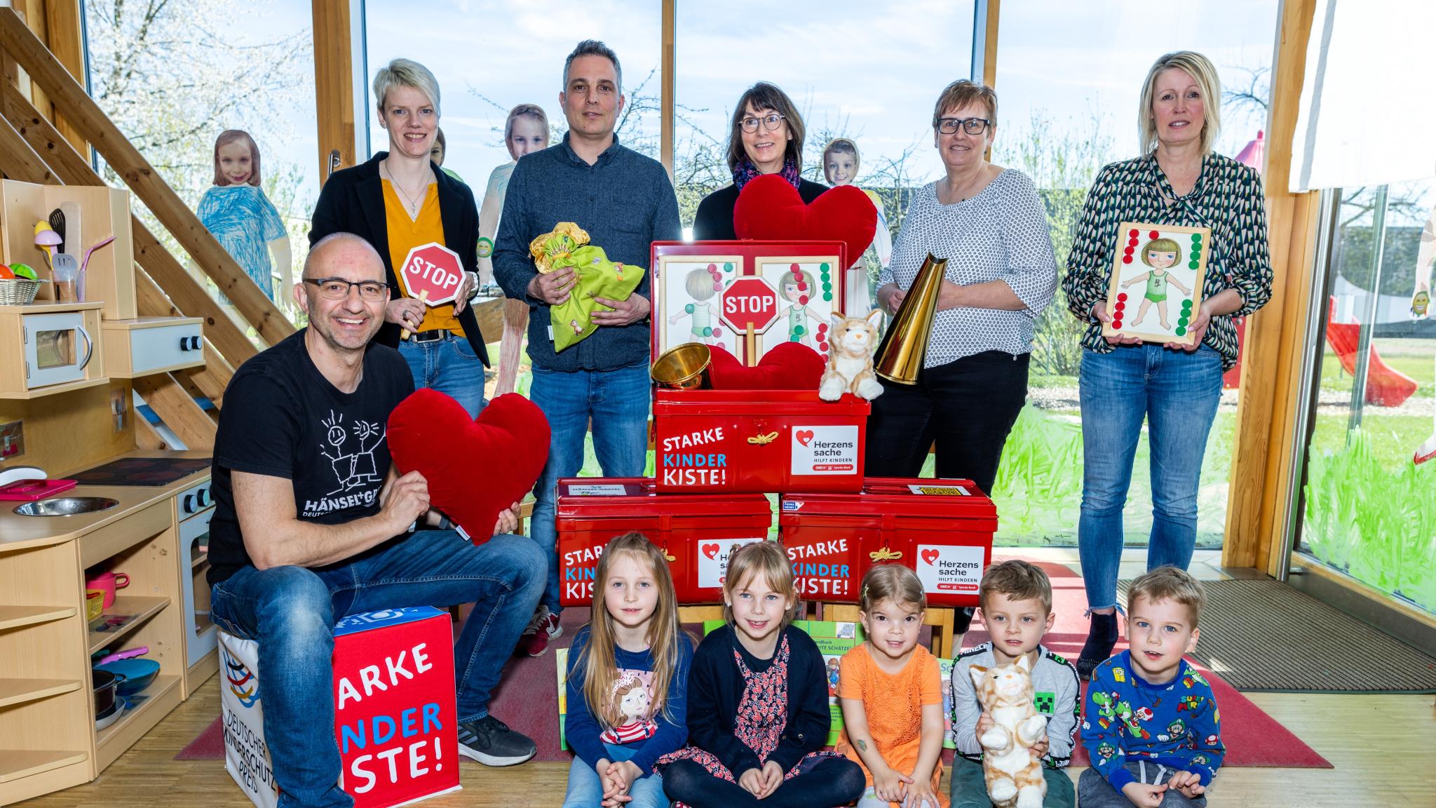 Kinder und Erwachsene mit Mini-STOP-Schildern, Spielsachen und einer Puppenküche