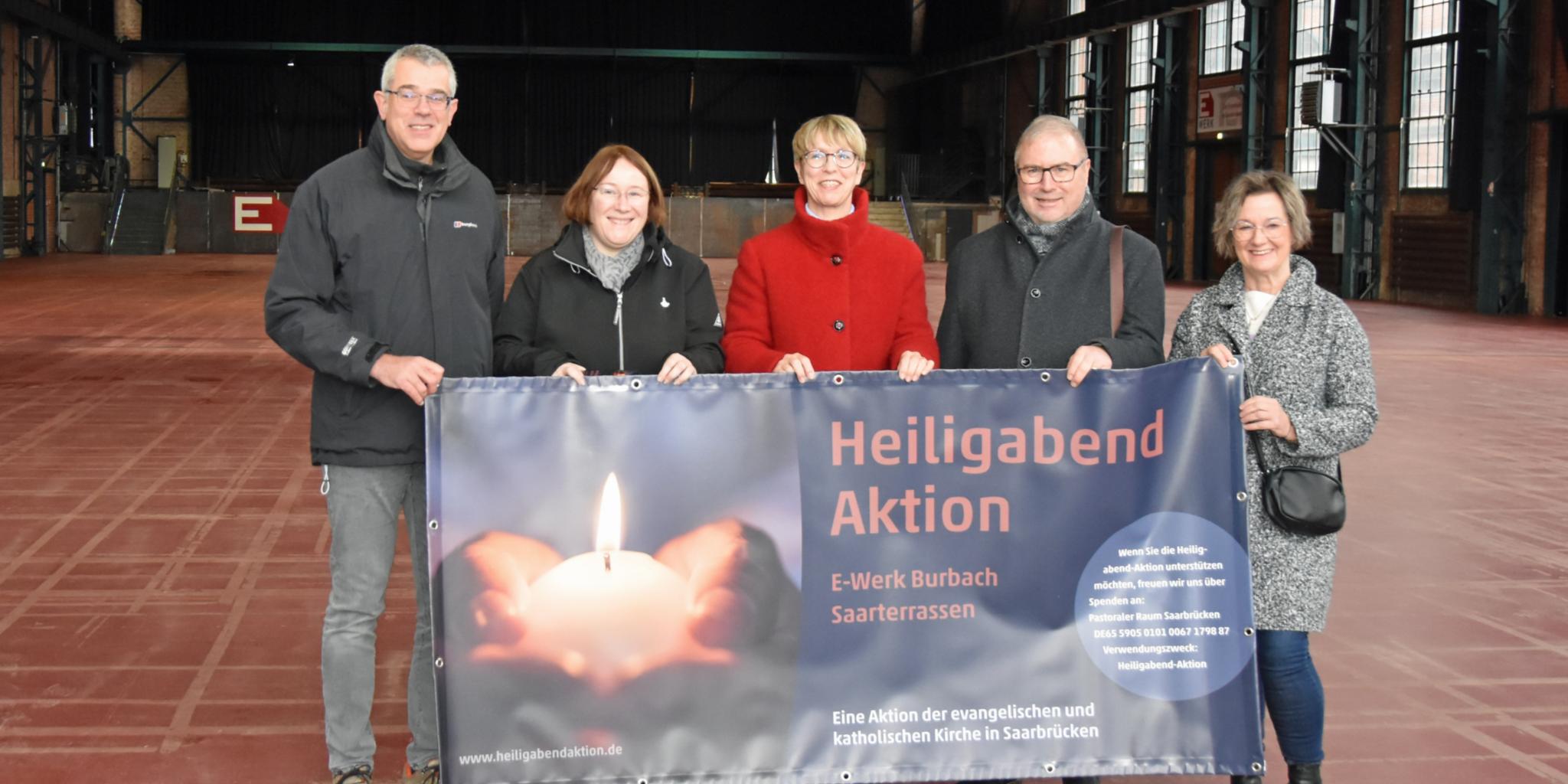 Fünf Personen stehen in einer Halle und halten das Plakat zur Heiligabend-Aktion.