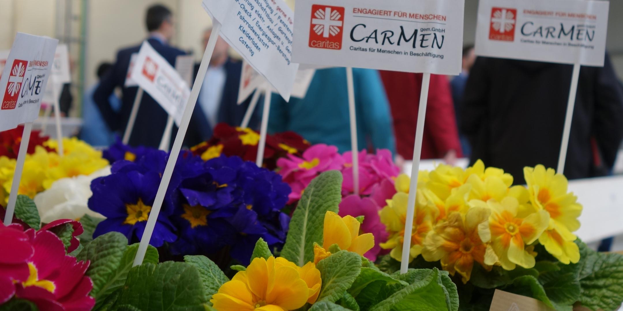 Blumen stehen auf einem Tisch, darin Zettel auf denen CarMen gGmbH steht.