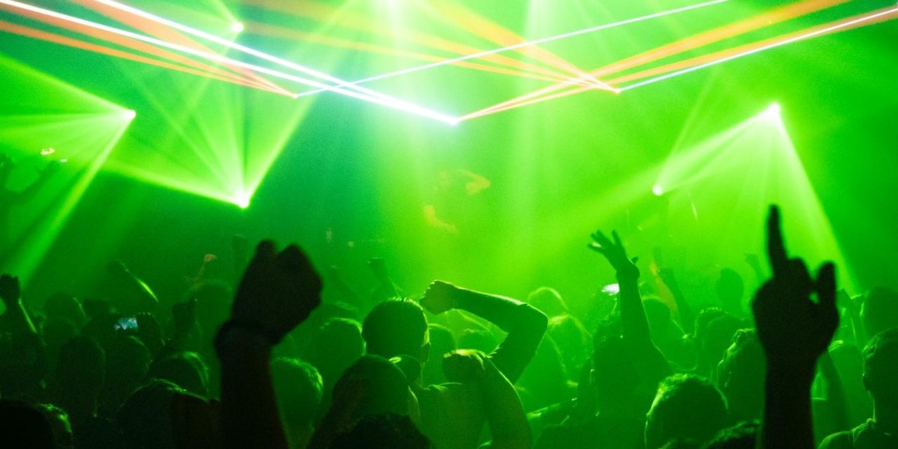 Tnanzende Menge im Club bei grünem Licht; im Hintergrund ein D.J.