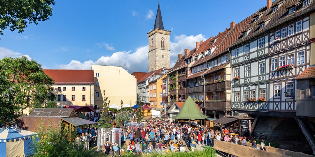 Foto der Altstadt Erfurt; viele Menschen flanieren bei Sonnenschein und blauem Himmel durch die Stadt.