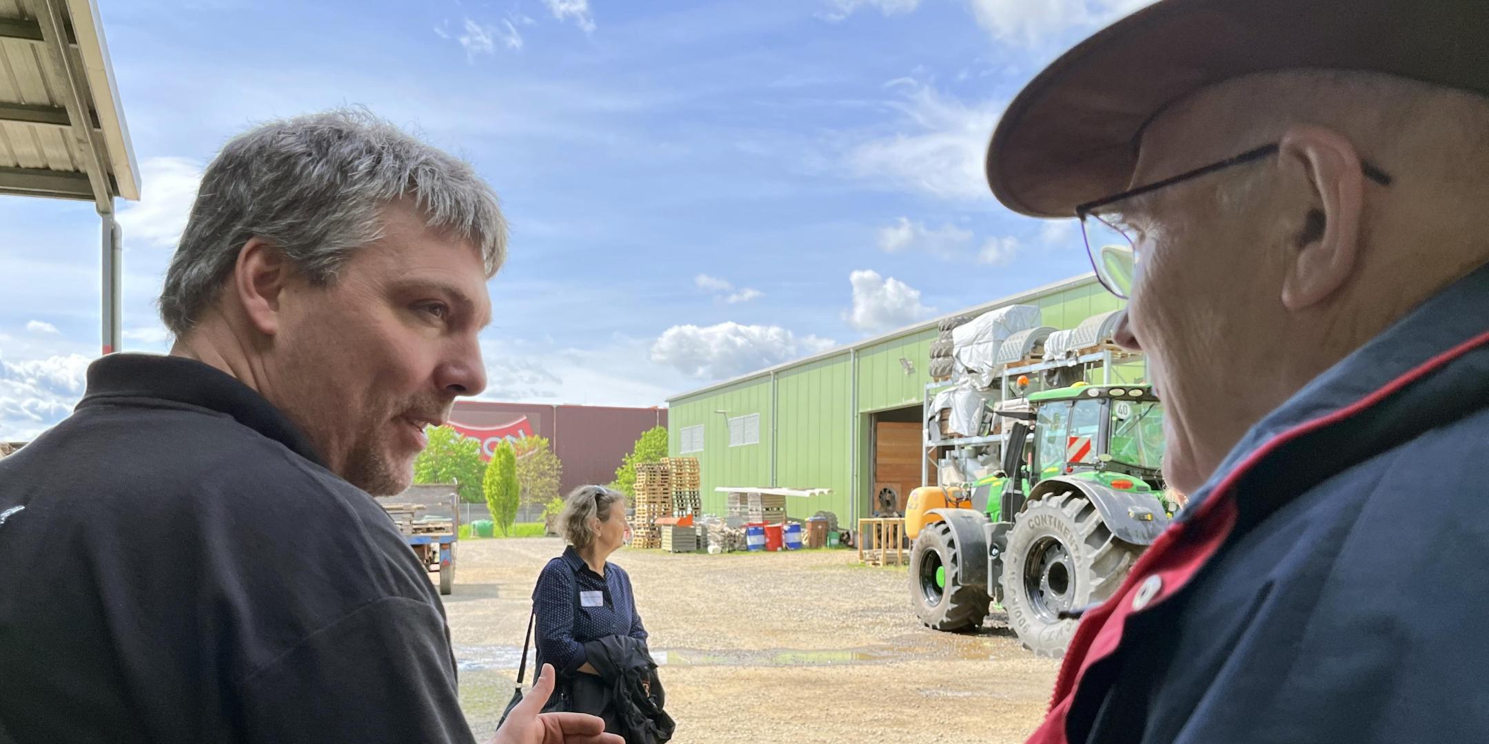 Zwei Männer im Gespräch, im Hintergrund ist ein Traktor zu sehen.