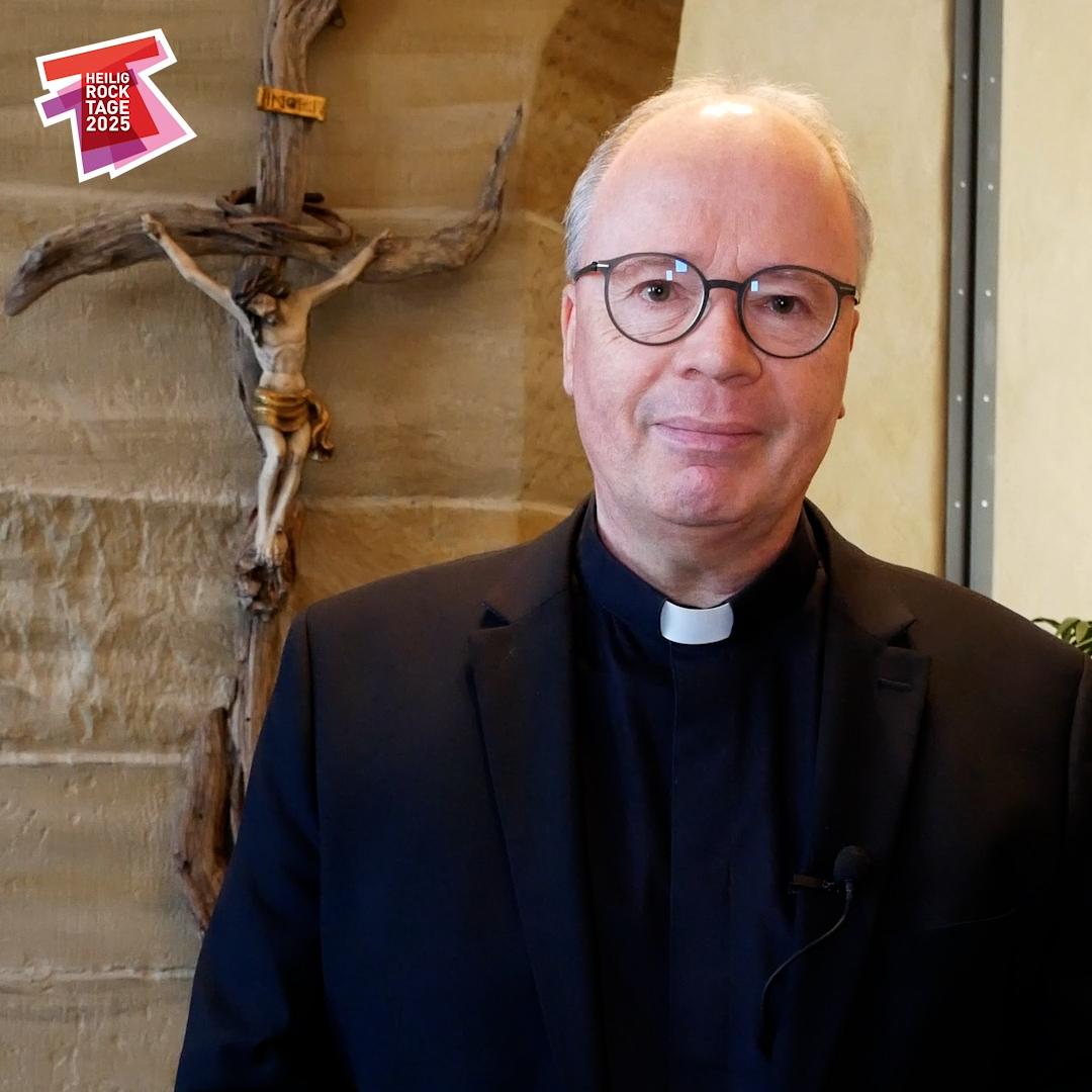 Bischof Ackermann steht neben einem Kruzifix. Links ist das Logo der Heilig-Rock-Tage. Darunter das Leitwort: Unglaublich - ich glaube