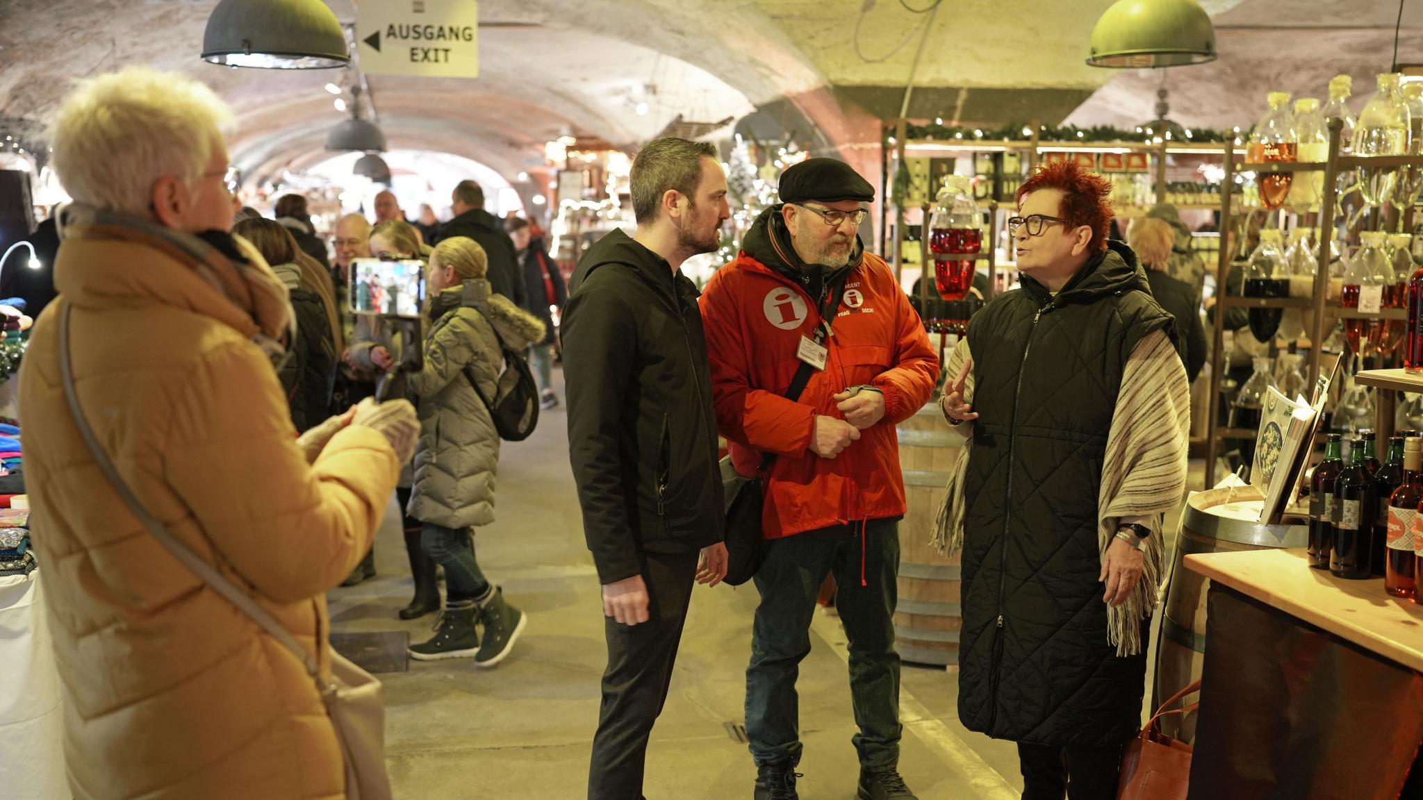 Gabriele Centurioni (rechts) und Tobias Schmitt treffen sich auf dem Wein-Nachts-Markt mit Gästeführer Günter Hauenstein (Zweiter von rechts). Monika Hochscheid (links) zeichnet das Video auf.