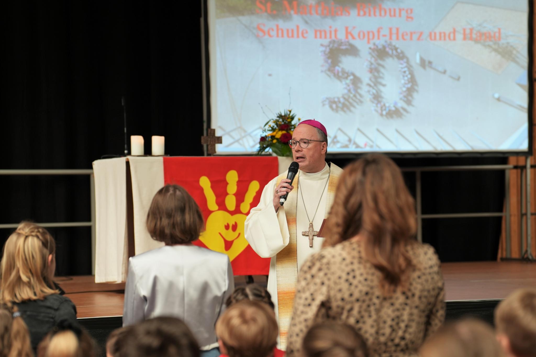 Der Bischof bezieht die Grundschulkinder in den Gottesdienst in der Turnhalle mit ein.