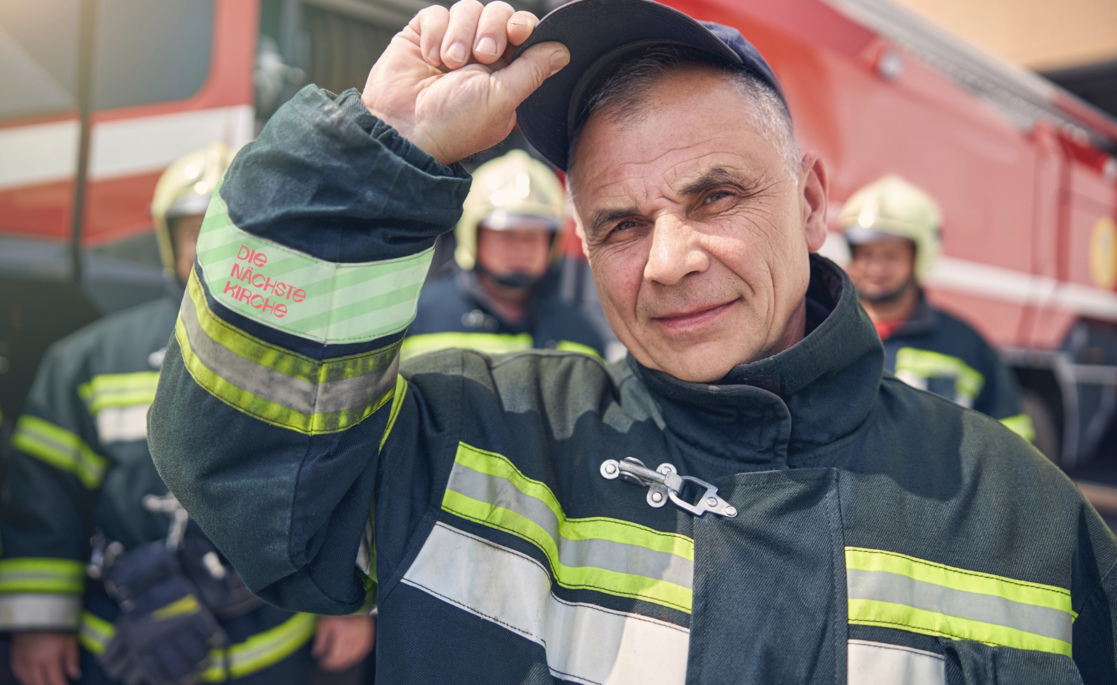 Feuerwehrmann fasst sich an Helm. Auf seinem Arm steht 'Nächste Kirche'