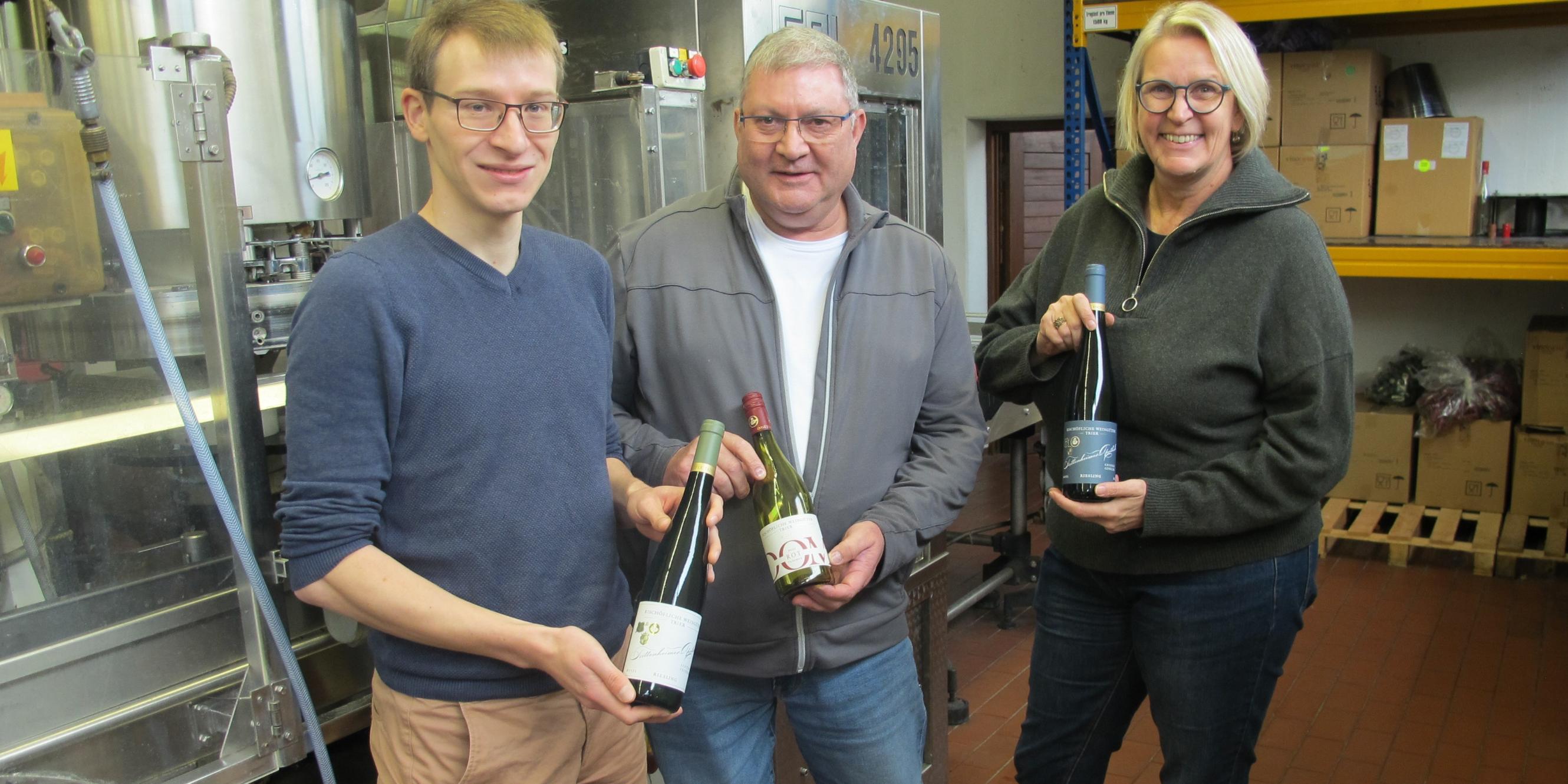 Lukas Böhm, Johannes Becker und Julia Lübcke mit Weinflaschen der Bischöflichen Weingüter in Trier. (vlnr.)