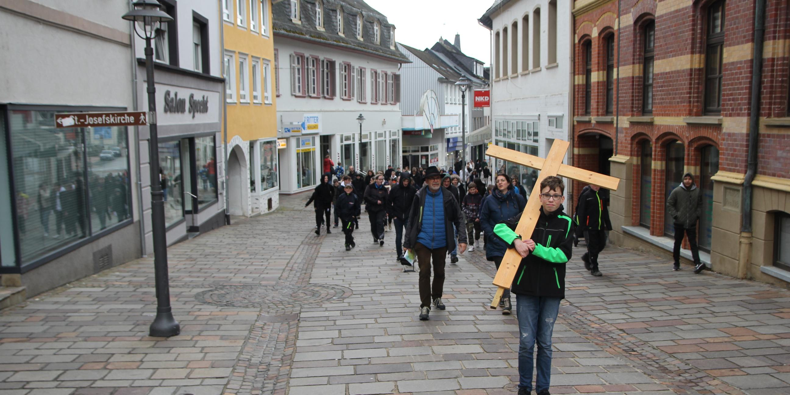 Ein Junge mit einem großen Kreuz zieht durch eine Fußgängerzone.