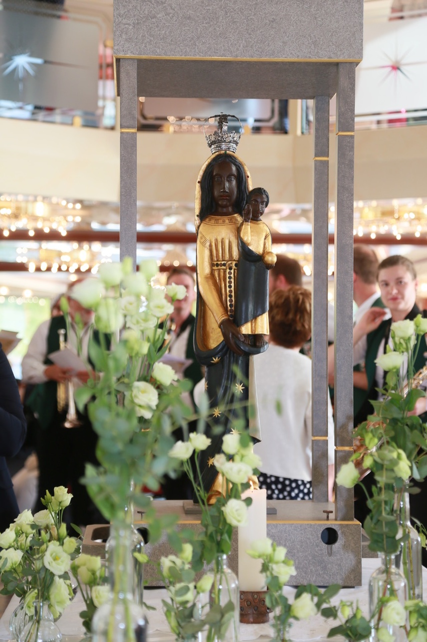Eine schwarze Madonna-Figur steht mit vielen Blumen in einem Schiff.