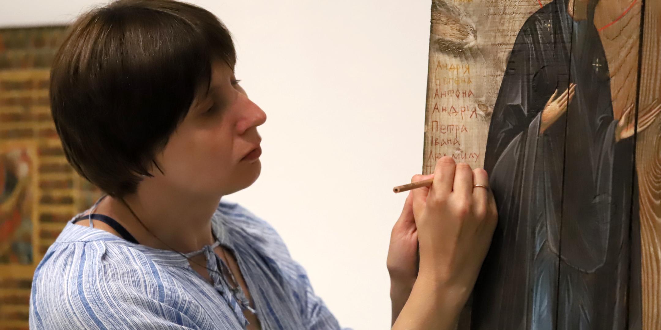Sofia Atlantova schreibt mit einem dünnen Buntmalstift den ersten Namen eines ukrainischen Kriegsopfers auf das raue Holz