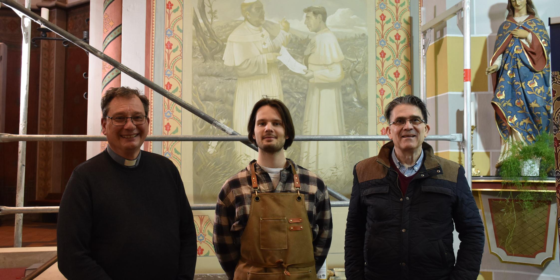 Pfarrer Peter Leick, Jonas Hammen und Patrik Feltes (von links) vor dem Bildnis, das bis Ende des Monats fertiggestellt sein soll.