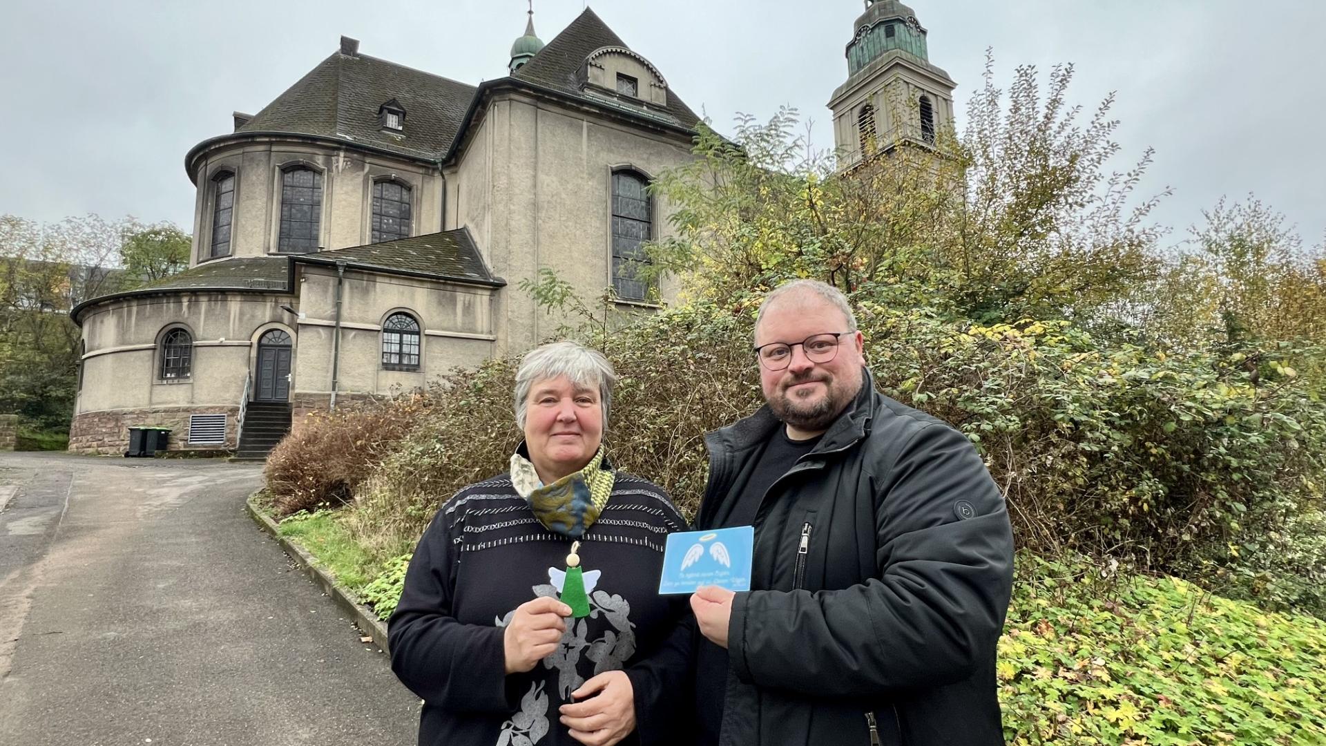 Zwei Menschen stehen vor einer Kirche und präsentieren eine Karte, die sie in der Hand halten