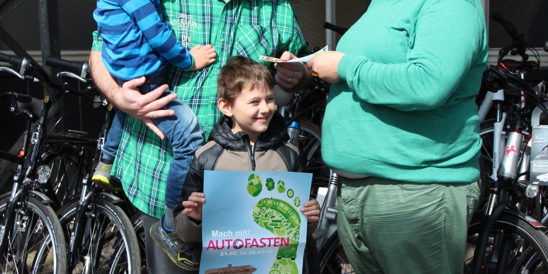 Autofaster Thomas Brausch freut sich mit Söhnen Anton (4, auf dem Arm) und Emil (8) über den Gutschein, den Johannes Wiegel (Aktion Autofasten, rechts) überreichte.