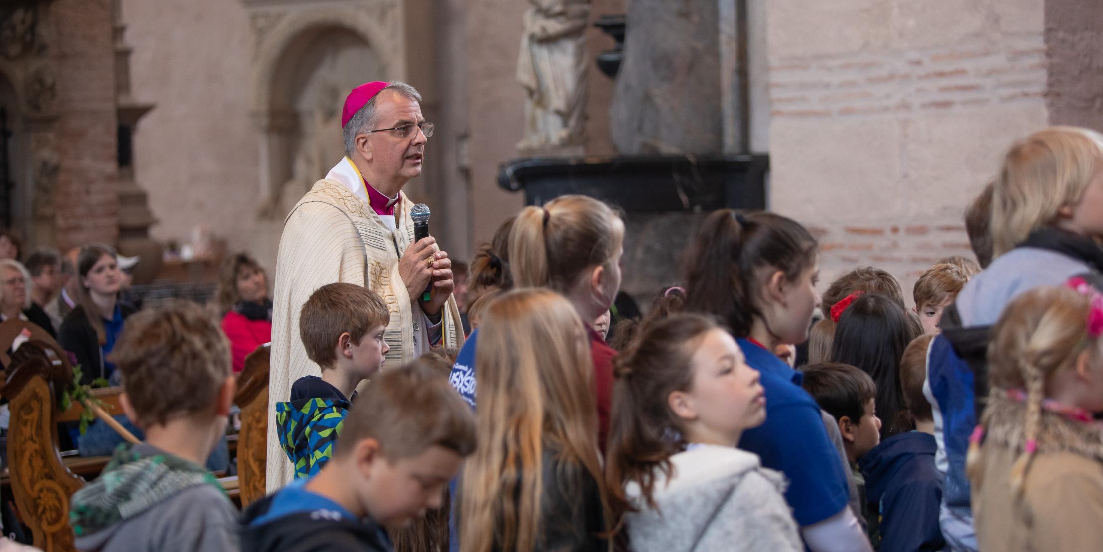 Weihbischof Peters und die Kinder betrachten zusammen das Kreuz.