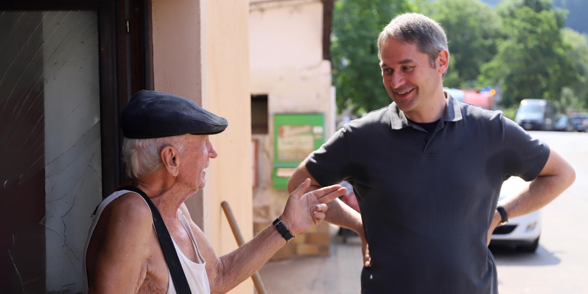 Pfarrer Kaufmann im Gespräch mit einem älteren Bewohner, der hilft, die Straßen zu säubern.