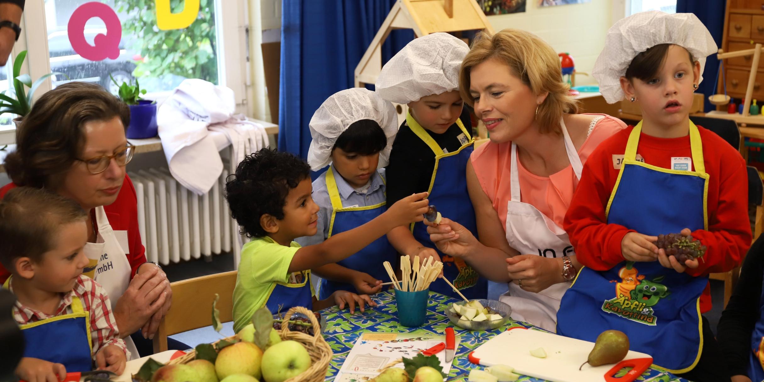 Bundesministerin Julia Klöckner und Kita gGmbH Trier-Geschäftsführerin Cordula Scheich bereiten in der Kita St. Simeon gesunde Snacks mit den Kindern zu.