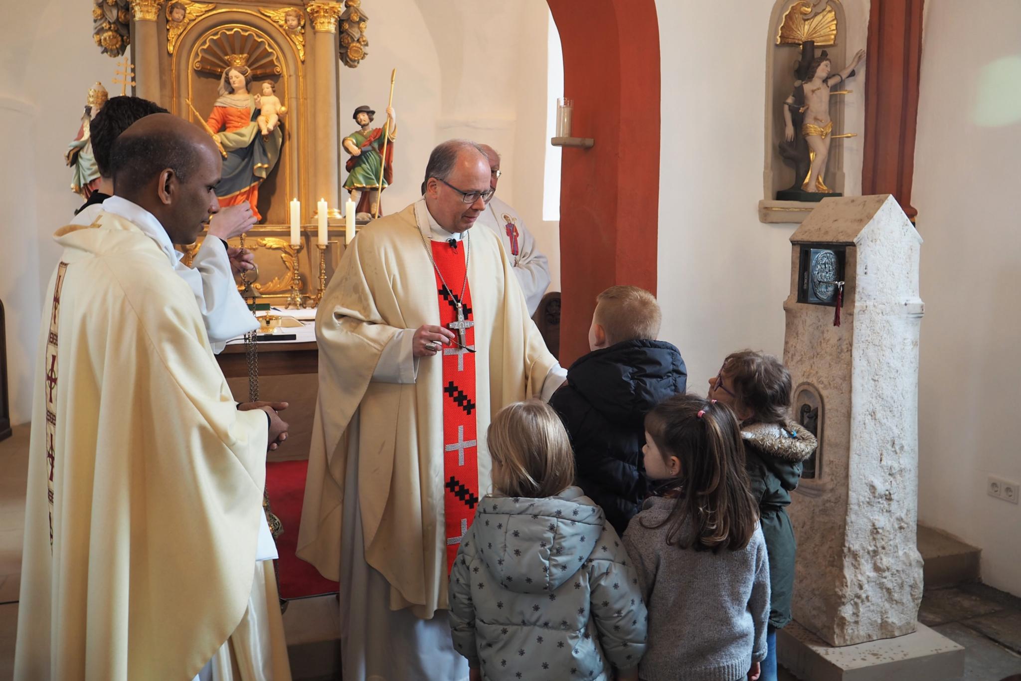 Bischof Ackermann (Mitte) bereitet mit Kindern aus der Gemeinde den Weihrauch vor, um den Tabernakel in der Stele (rechts) zu segnen.