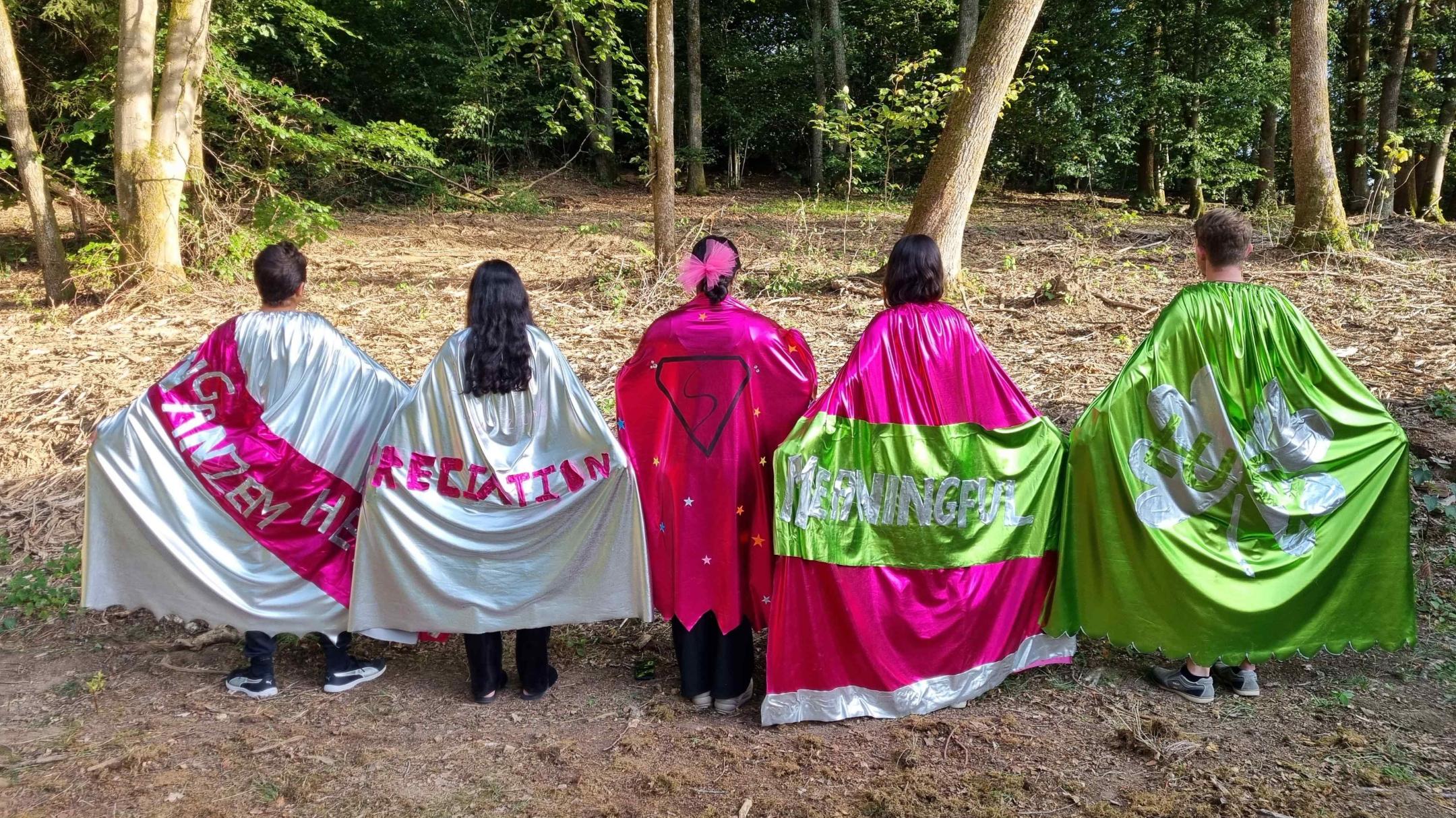 Junge Menschen von hinten mit glitzernden Umhängen.