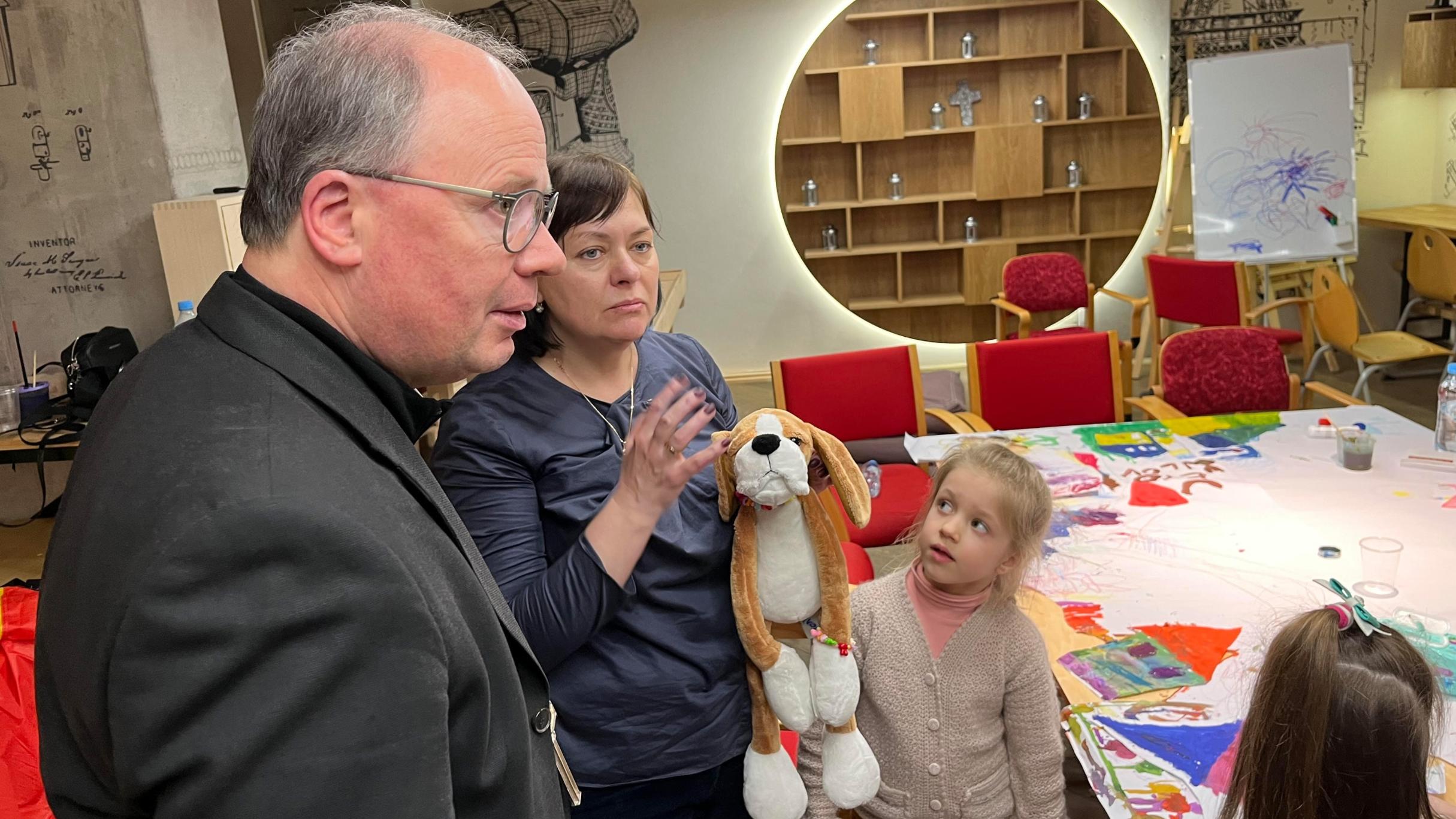 Der Bischof zu Besuch in einem Treffpunkt der Malteser, wo geflüchtete Kinder spielen können. Zu Beginn bekommen sie ein Stofftier überreicht, das sie auch umhängen können und das das Gefühl der Geborgenheit geben soll