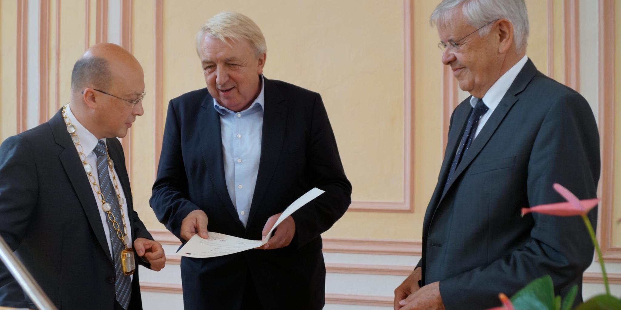 Johannes Brantl, Rektor der Theologischen Fakultät Trier, (links) und Herbert Hoffmann, Vorsitzender der Peter-Wust-Gesellschaft, (rechts) überreichen den Peter-Wust-Preis an den Schriftsteller Hanns-Josef Ortheil.