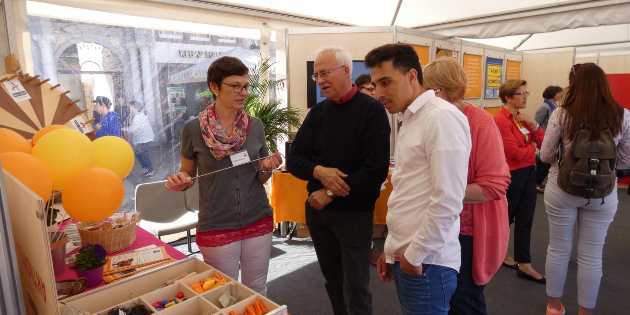 Andrea Steyven (links) zeigt Besuchern des Informationszeltes, welche Produkte in den Beschäftigungs- und Qualifizierungsmaßnahmen – hier ein Schwenkerwender – gefertigt werden.