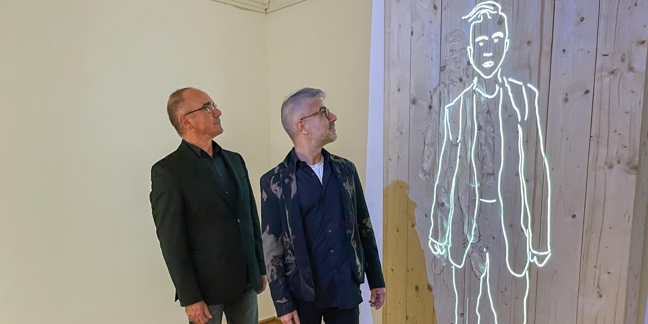 Medienkünstler Burkhard Detzler (links) und Mert Akbal blicken auf die von ihnen mit KI generierte Silhouette von Willi Graf in der Ausstellung.